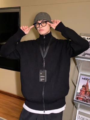Front view of a men's black ribbed full-zip cardigan sweater with high stand collar, exposed zipper, glasses, and layered streetwear outfit