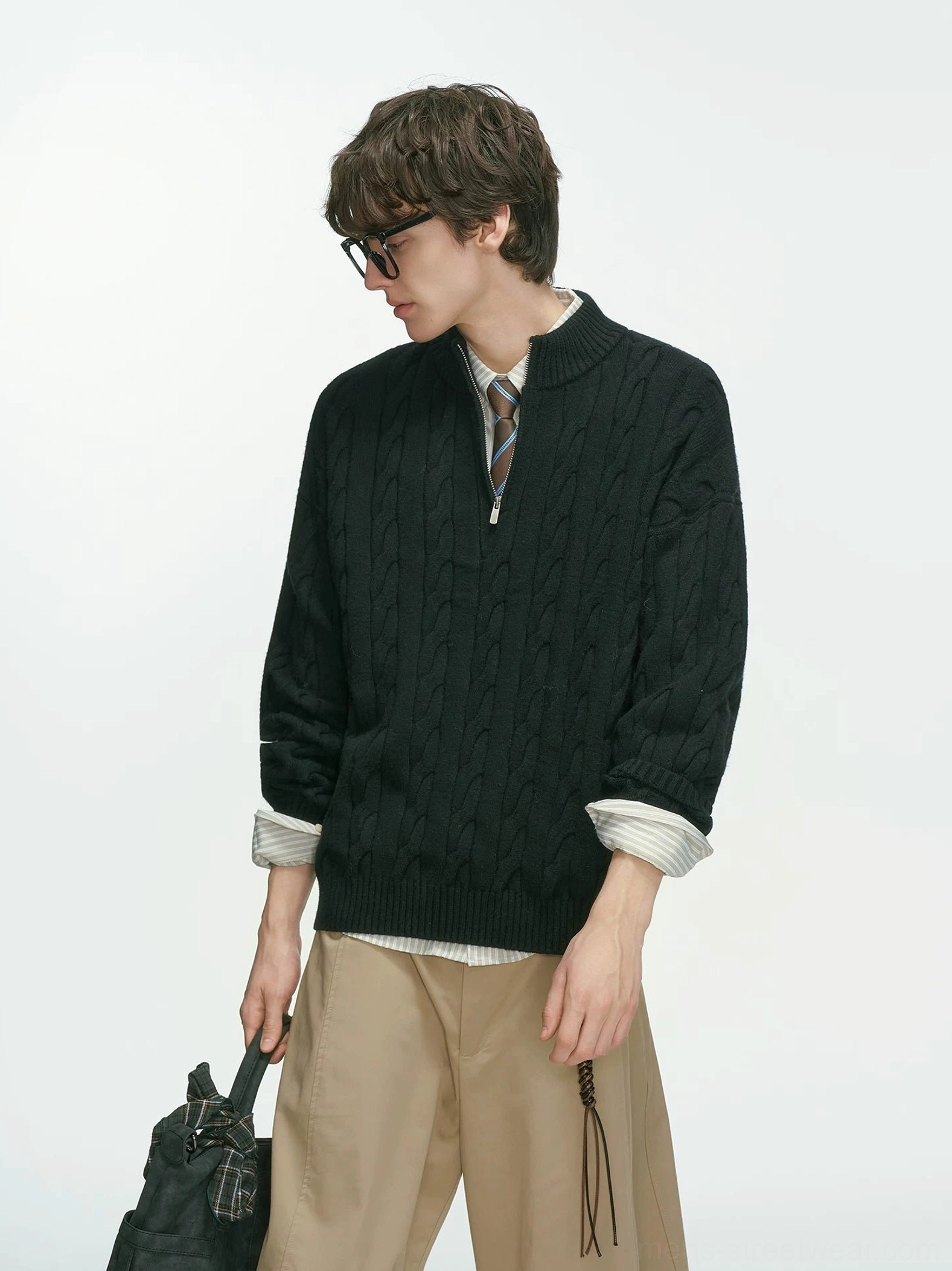 Side profile of a black cable knit half-zip sweater for men with layered shirt cuffs and wide-leg khaki trousers