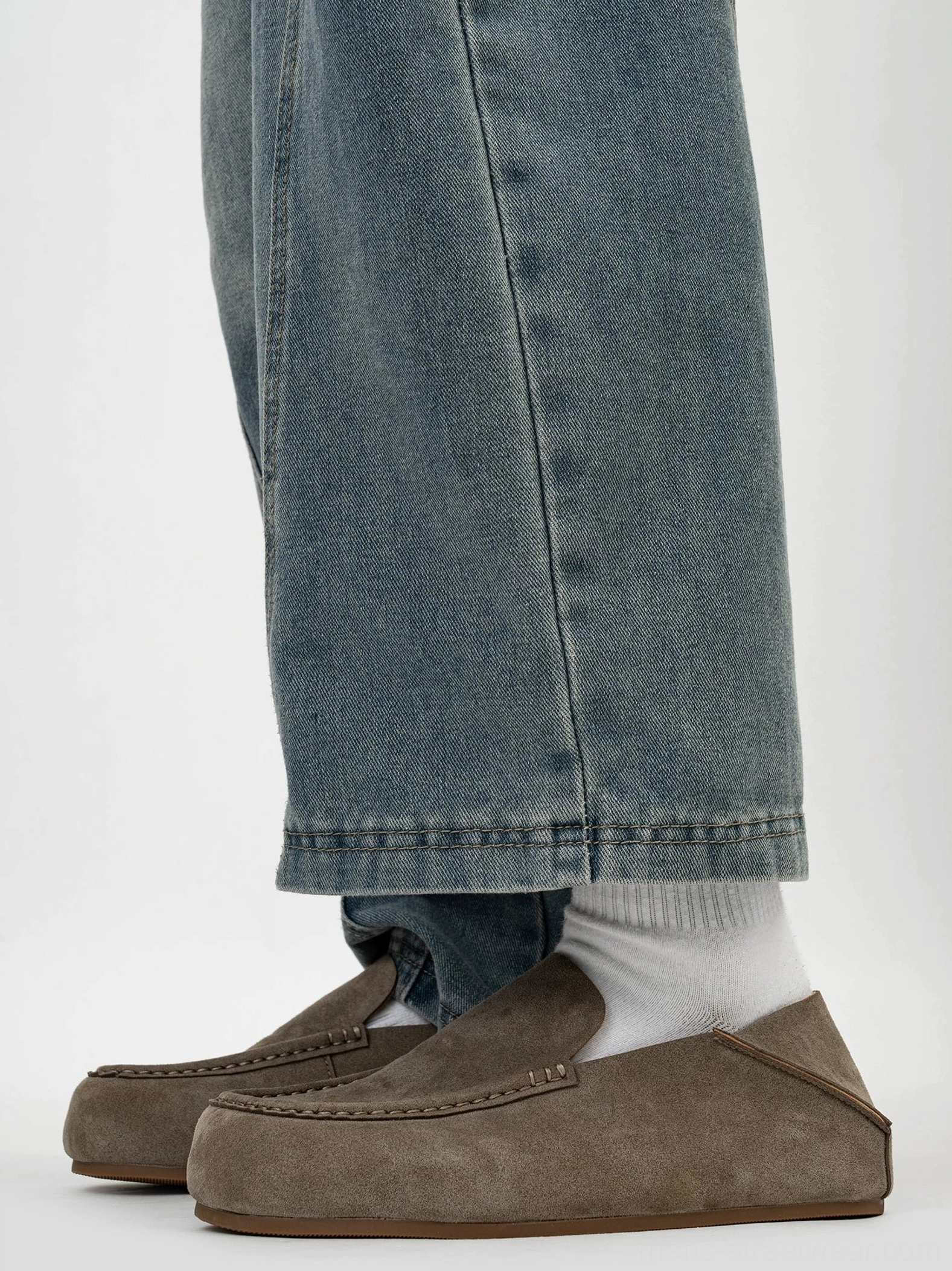 Men's casual suede loafers worn with blue jeans and white socks showing the low cut vamp and flat rubber outsole
