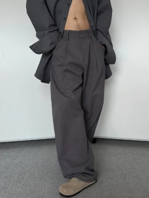Three-quarter front view of men's charcoal grey wide-leg pleated trousers styled with a tonal open grey shirt and side pockets