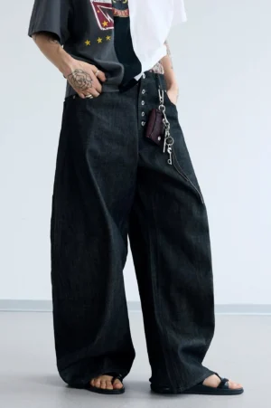 Three-quarter front view of men's oversized curved wide-leg black jeans showing the plaid inner waistband and relaxed streetwear fit