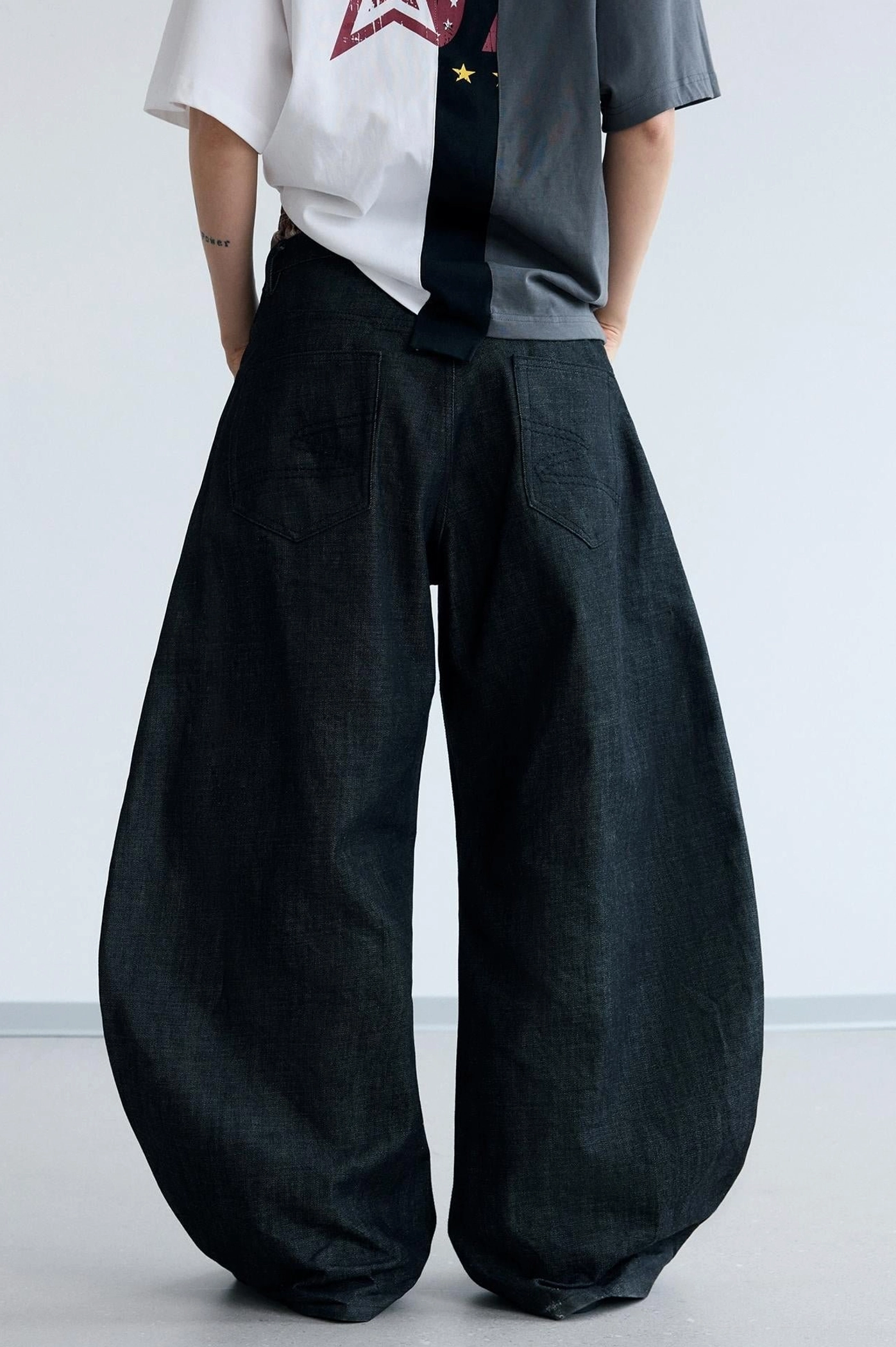 Back view of men's dark black curved knife jeans with an oversized rounded wide-leg silhouette for Korean streetwear styling