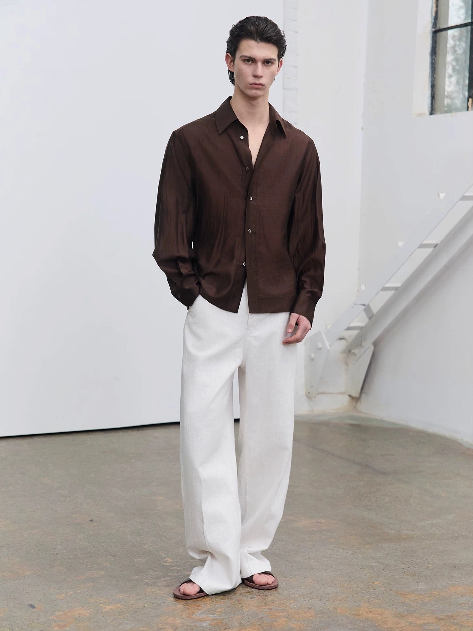Men's dark brown semi-sheer fluid sheen tailored shirt shown from the front with pointed collar, button placket, long sleeves, and softly shaped waist in a Korean streetwear outfit