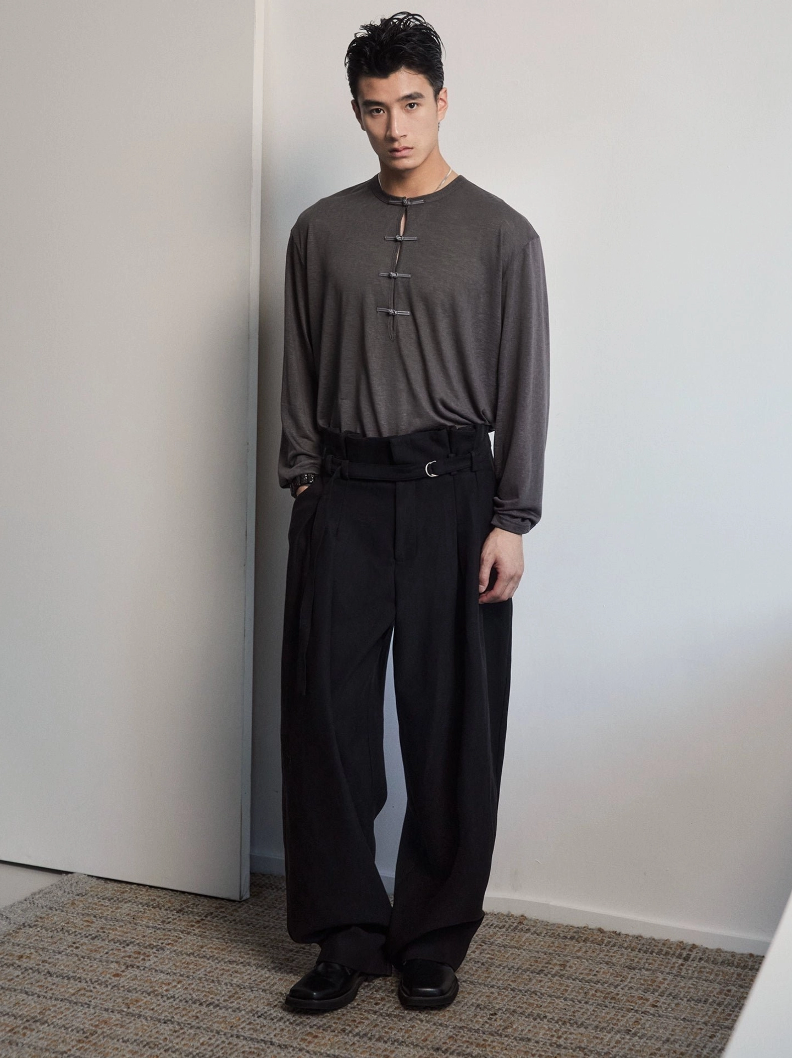 Men's dark gray relaxed fit frog button Henley long sleeve tee styled with black wide leg trousers in studio