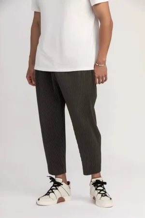 Dark gray men's pleated cropped pants with relaxed tapered fit, elastic waistband, white T-shirt, and casual sneakers in a studio streetwear outfit