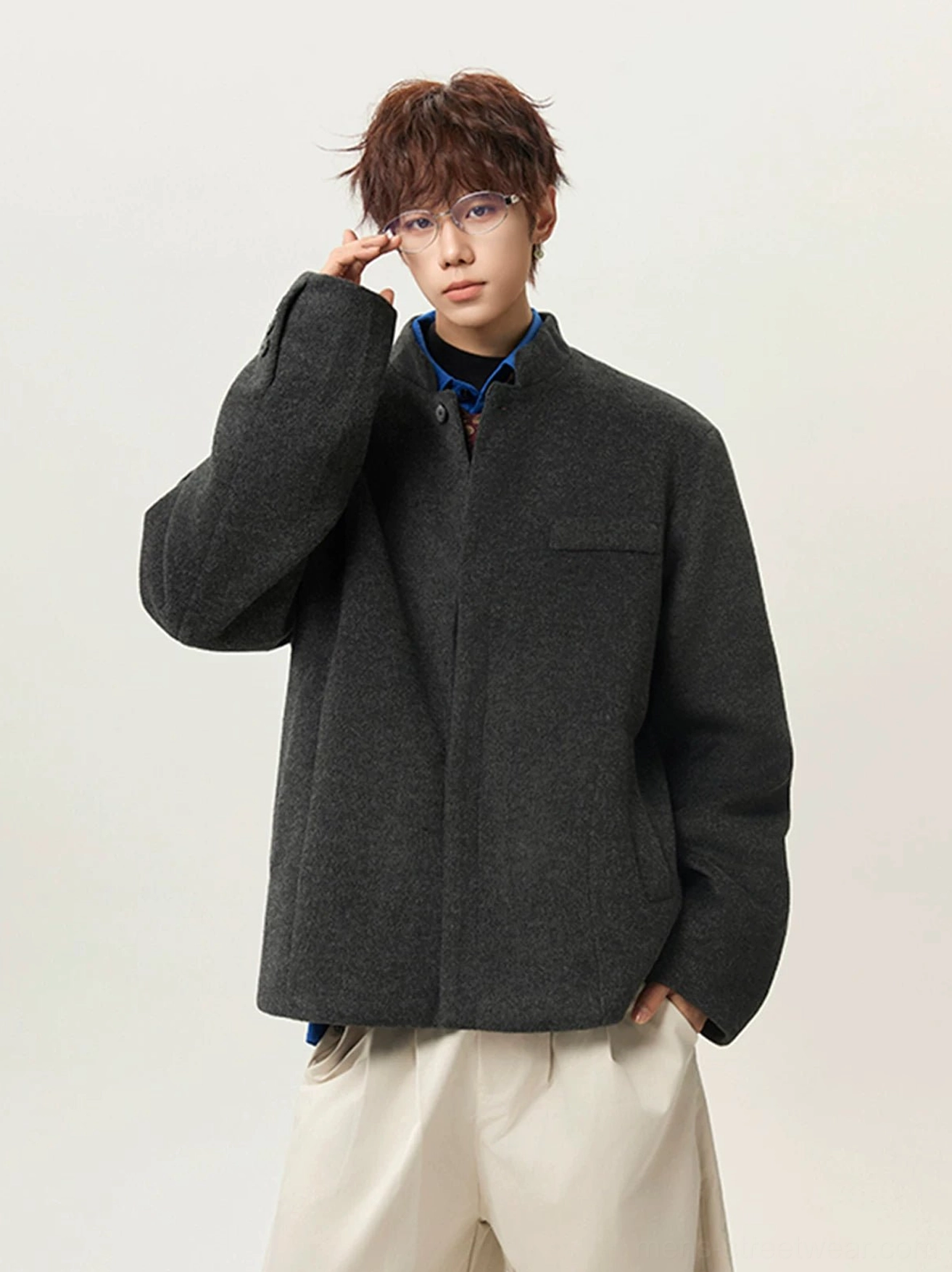 Dark gray men's stand collar wool blend jacket front three quarter view with concealed placket chest pocket and off white wide leg pants