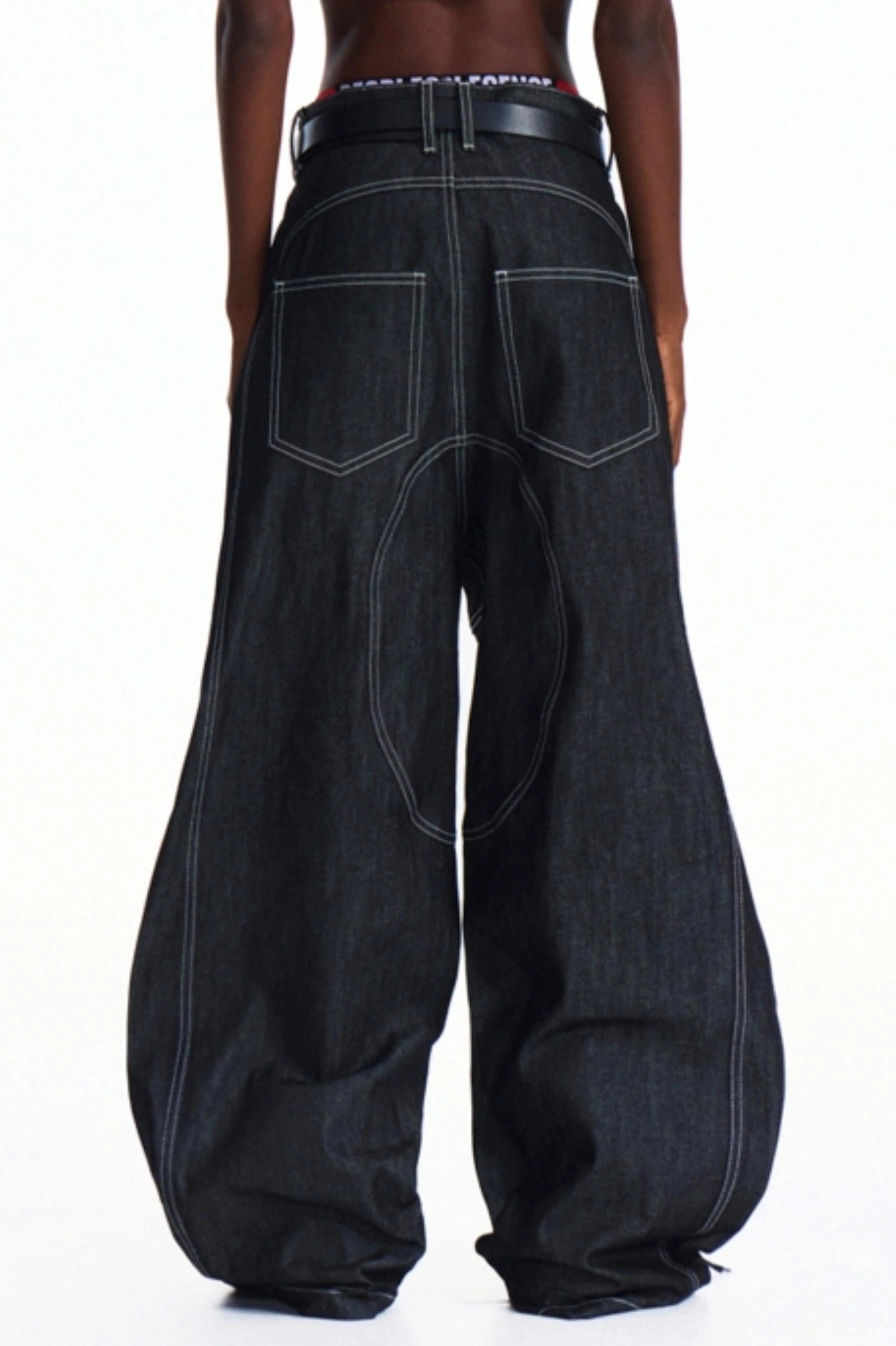 Rear view of men's dark wash wide-leg denim pants showing classic back pockets, contrast white topstitching, and loose streetwear silhouette