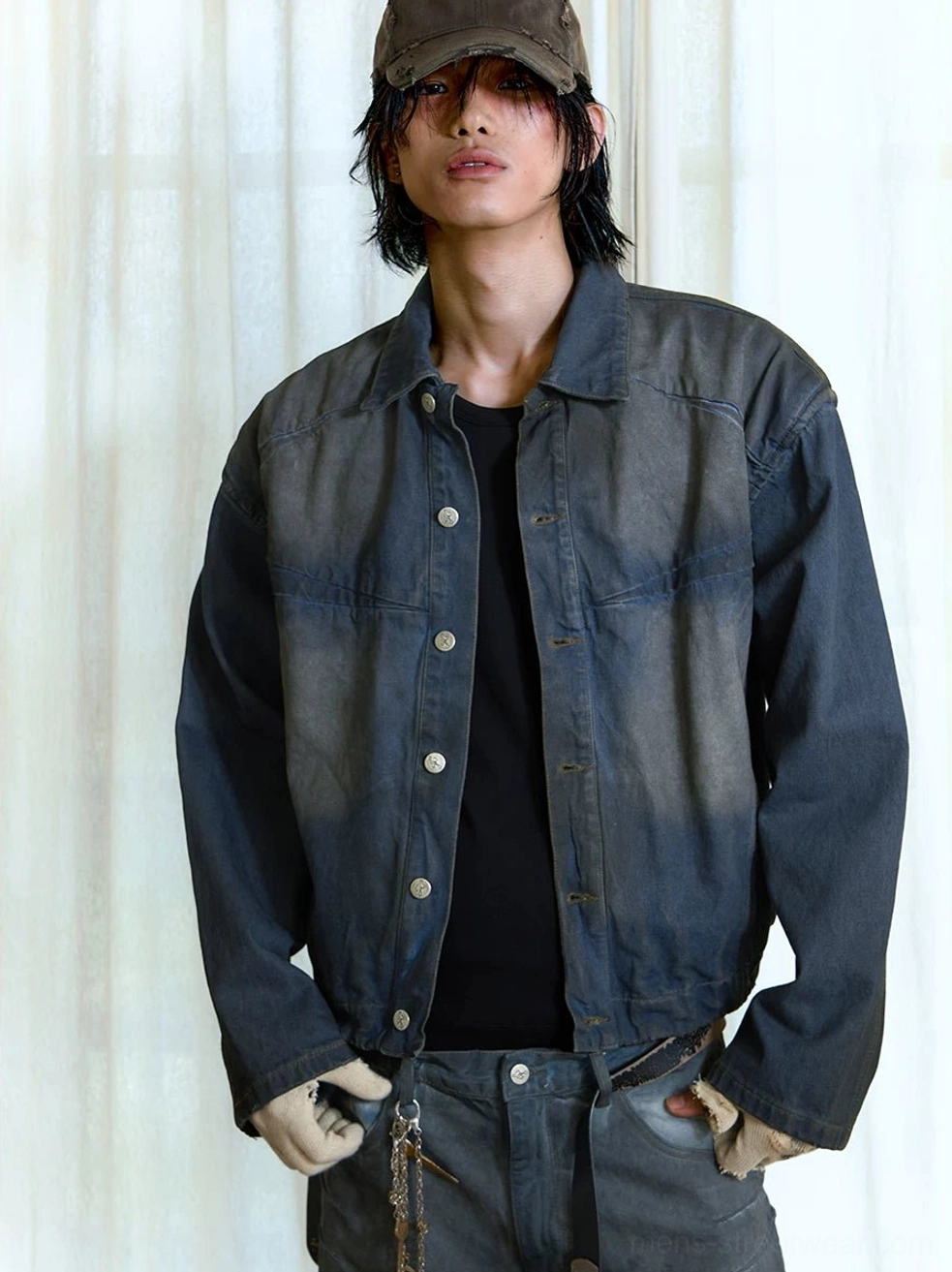 Male model wearing men's faded indigo panel denim trucker streetwear jacket with matching washed jeans, black shirt, baseball cap and metal chain