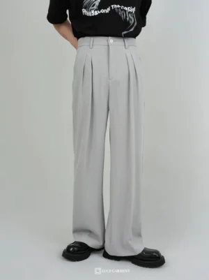 Men wearing gray pleated wide-leg trousers with a high waist, black graphic T-shirt, and black platform loafers in a studio