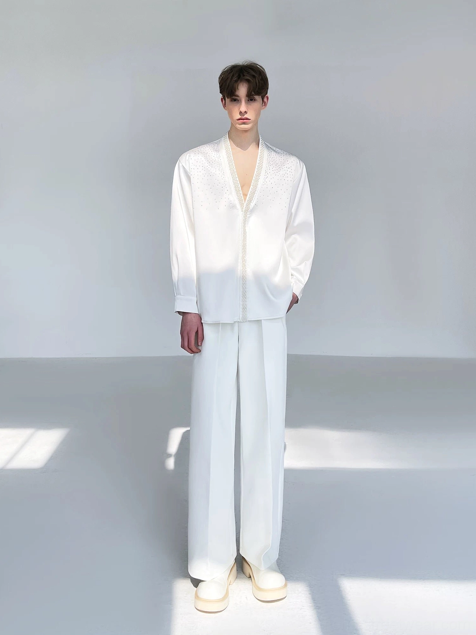 Full-body front view of a men's ivory satin deep V-neck shirt paired with high-waisted wide-leg white pants for an elevated Seoul fashion look