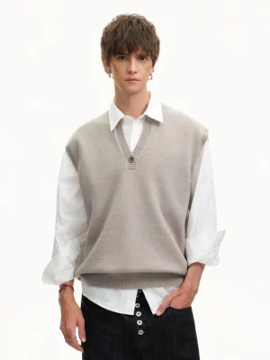 Men's light beige Henley knit vest layered over a white shirt with black jeans in a minimalist Korean streetwear outfit