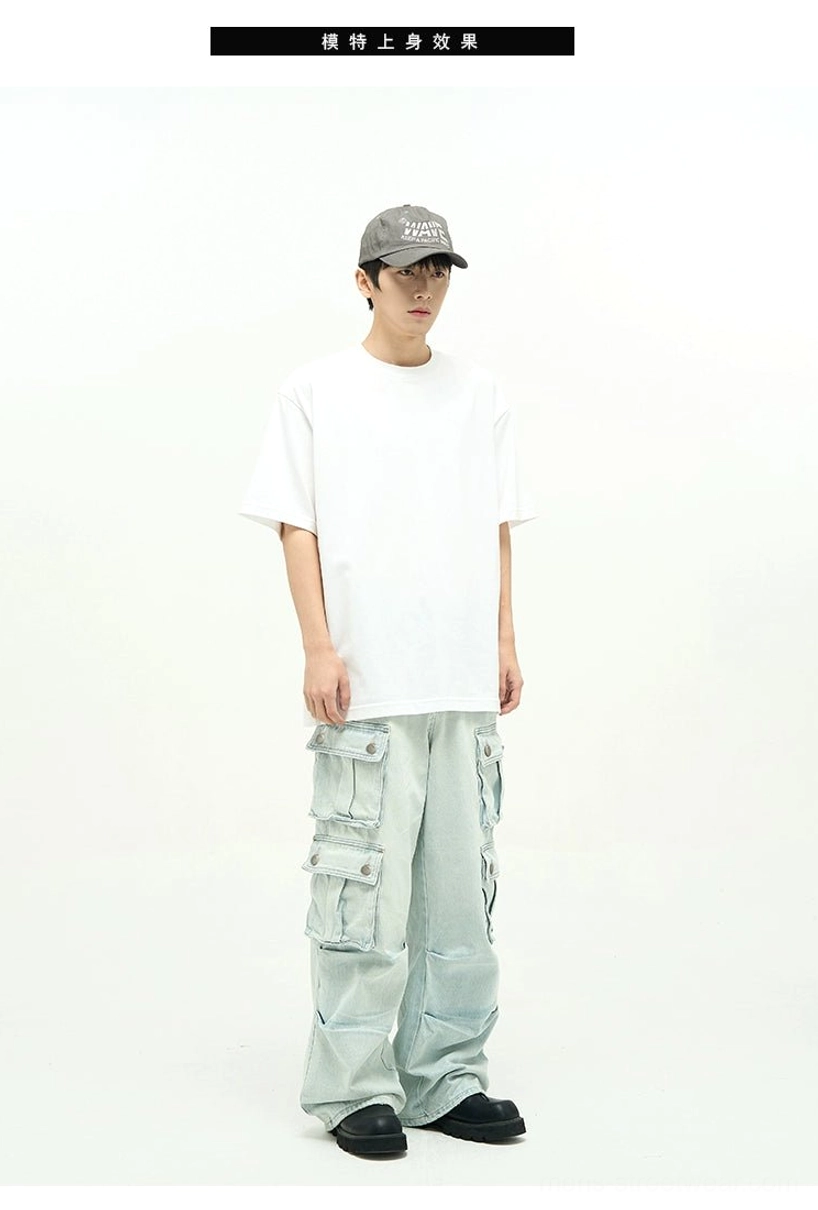 Male model wearing relaxed light blue cargo jeans with oversized side pockets, wide legs, white T-shirt, cap, and casual streetwear shoes