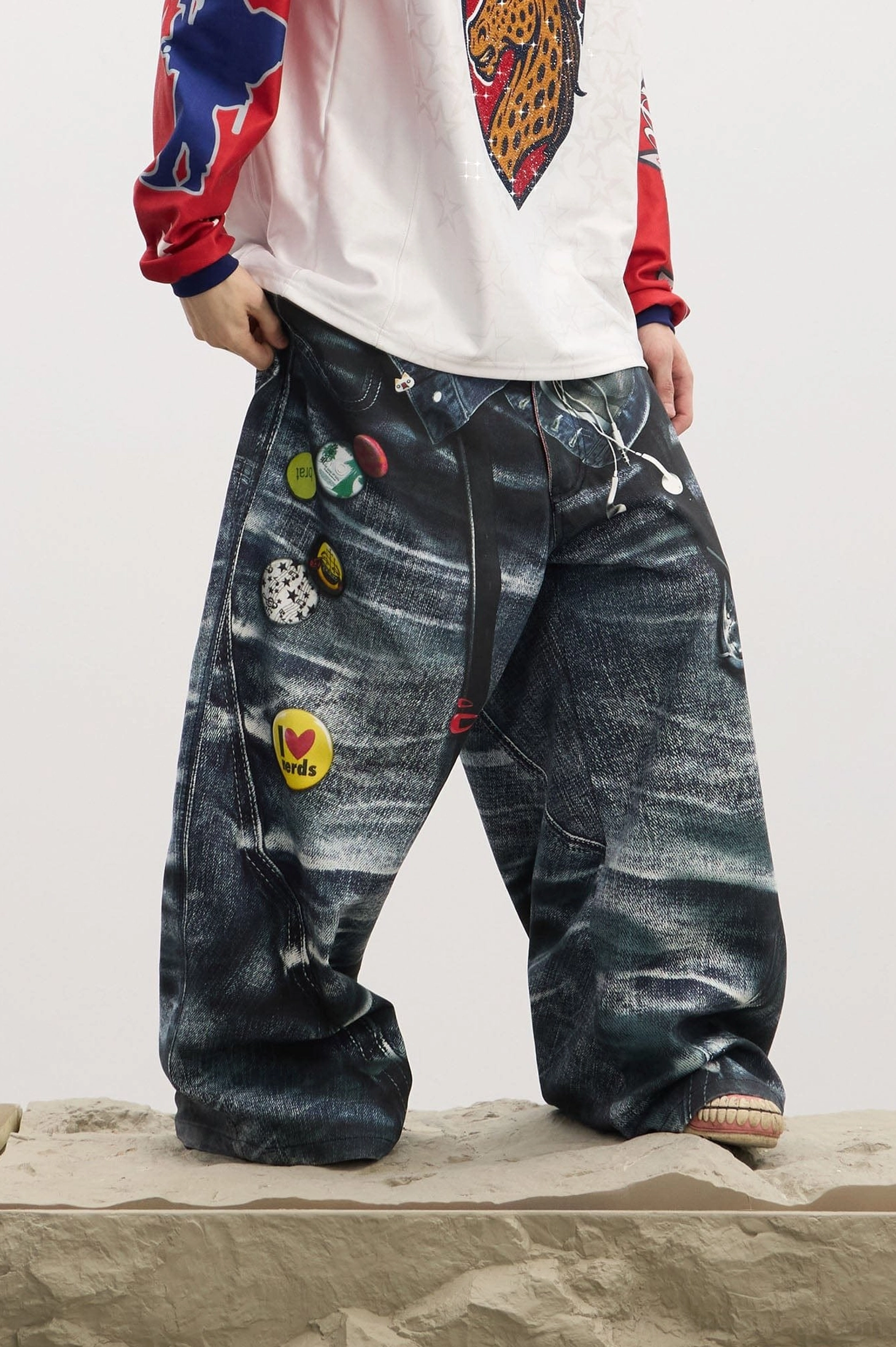 Close front-side view of men's loose wide-leg jeans with multiple decorative enamel-style pins and bold contemporary streetwear detailing