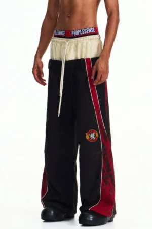 Men's loose wide-leg sport trousers shown from a three-quarter front angle with red outer panels, contrast trim, exposed drawstring waist, and embroidered thigh detail