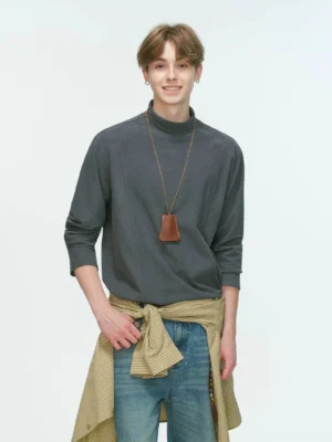 Charcoal gray men's mock neck long sleeve top styled with a leather pendant necklace and shirt tied around the waist in a Korean streetwear outfit