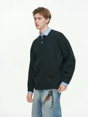 Men's navy blue relaxed knit polo sweater with drop shoulders layered over a blue striped shirt and styled with light wash jeans
