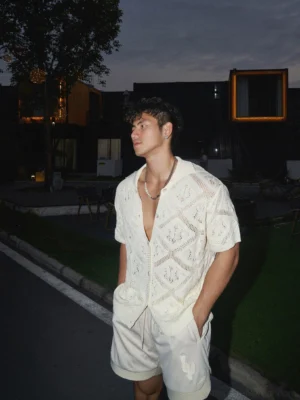 Men's off-white crochet button-up shirt with diamond knit texture styled in Korean streetwear at an outdoor industrial night setting
