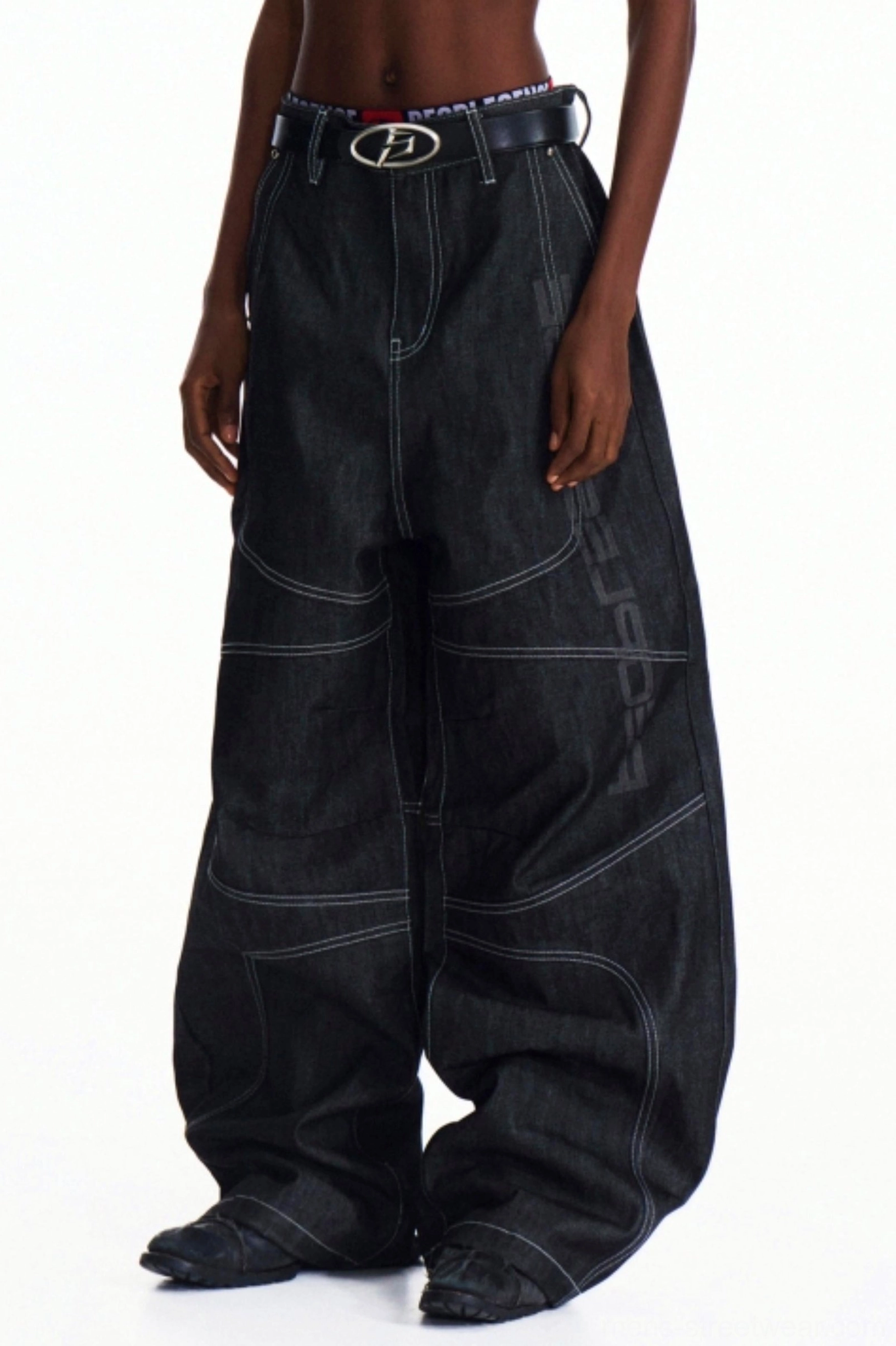 Three-quarter view of oversized men's dark denim wide-leg pants with relaxed Korean streetwear proportions, detailed stitching, and dark belt styling