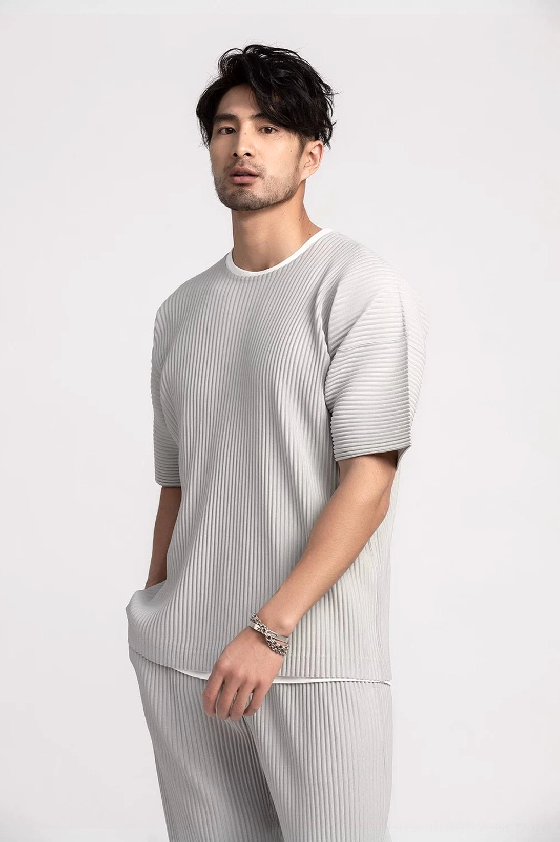 Side view of a relaxed men's pleated tee showing loose boxy fit and vertical textured fabric