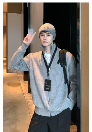 Male model wearing a light grey men's ribbed full-zip cardigan sweater with stand collar, backpack, beanie, and relaxed Korean streetwear styling