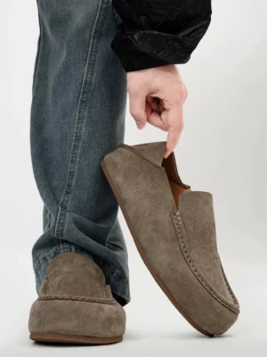 Men's taupe suede moc toe loafers styled with blue jeans and black outerwear in a low side three quarter view