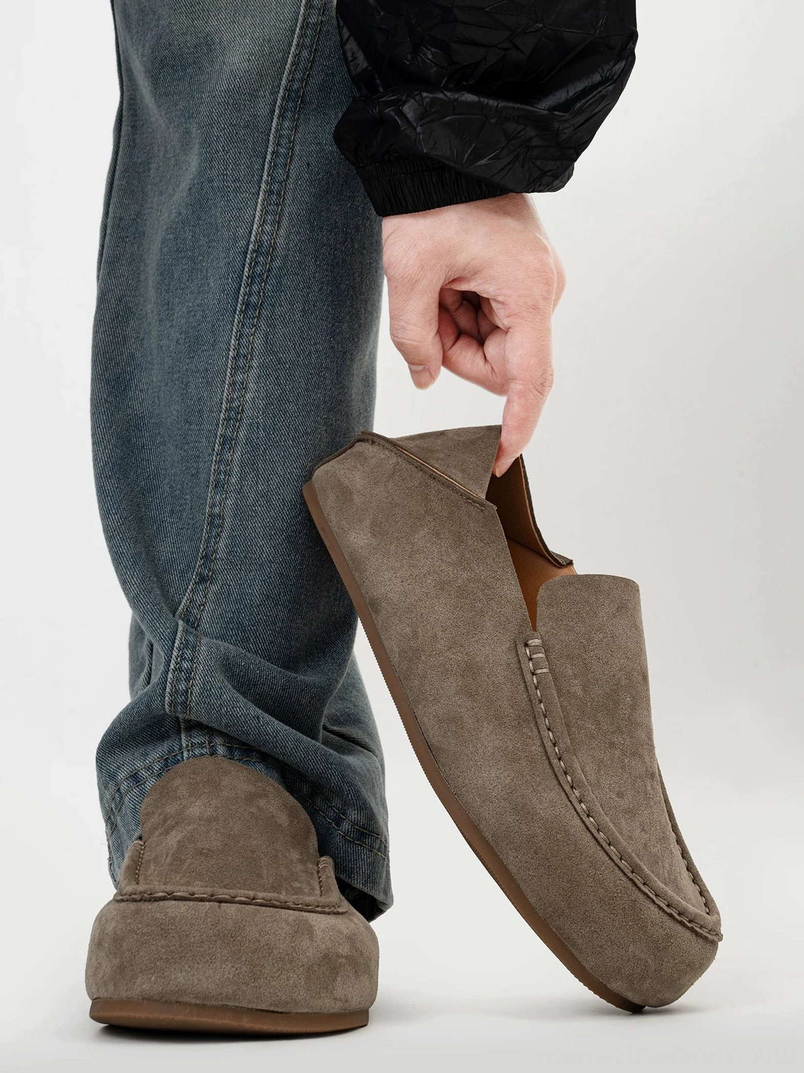 Men's taupe suede moc toe loafers styled with blue jeans and black outerwear in a low side three quarter view