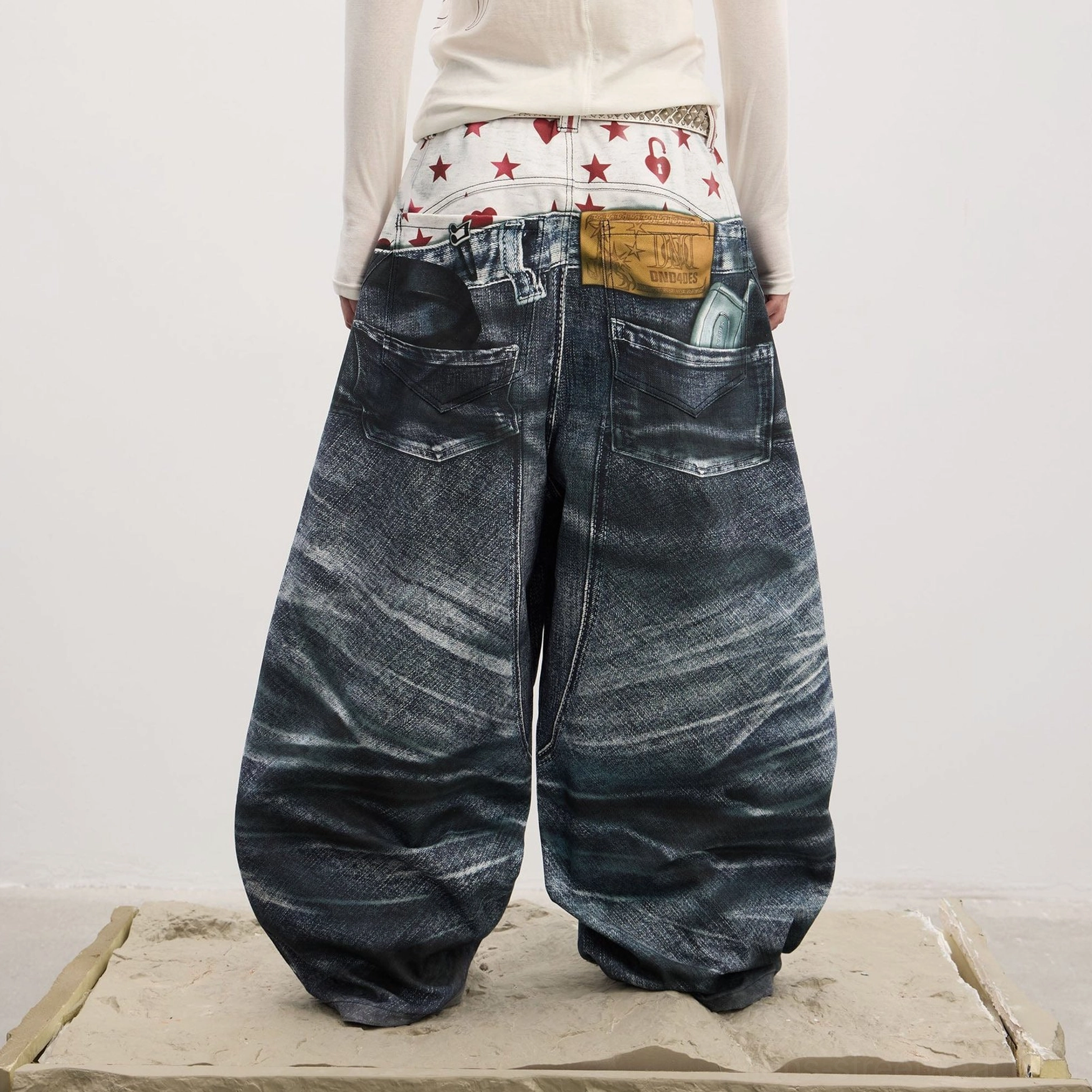 Back full-body view of men's ultra-baggy wide-leg denim jeans showing faux back pockets, leather-look tag, dark washed finish, and oversized streetwear silhouette