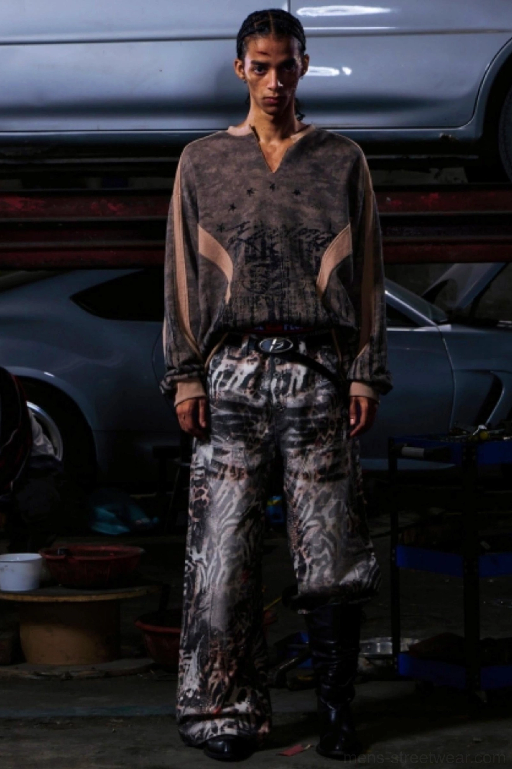 Men's vintage khaki camouflage half-zip pullover styled with zebra print cargo pants in an industrial workshop setting