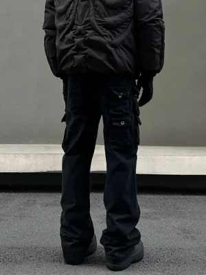 Rear low-angle view of men’s washed black multi-pocket flared cargo jeans styled with a black puffer jacket in an urban street setting