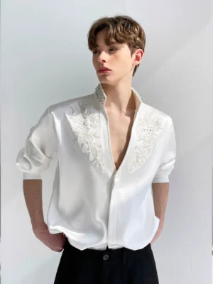 Men's white floral embroidered satin V-neck shirt styled with black tailored trousers in a front full upper-body view