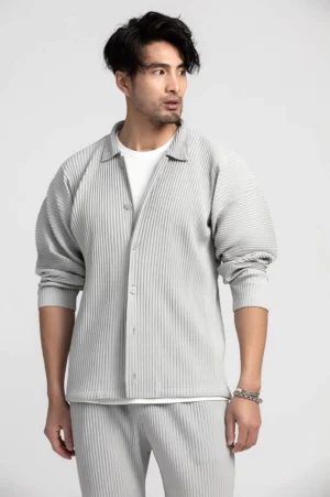 Men's relaxed white gray pleated button-up shirt with rolled sleeves styled with matching trousers in a minimalist studio