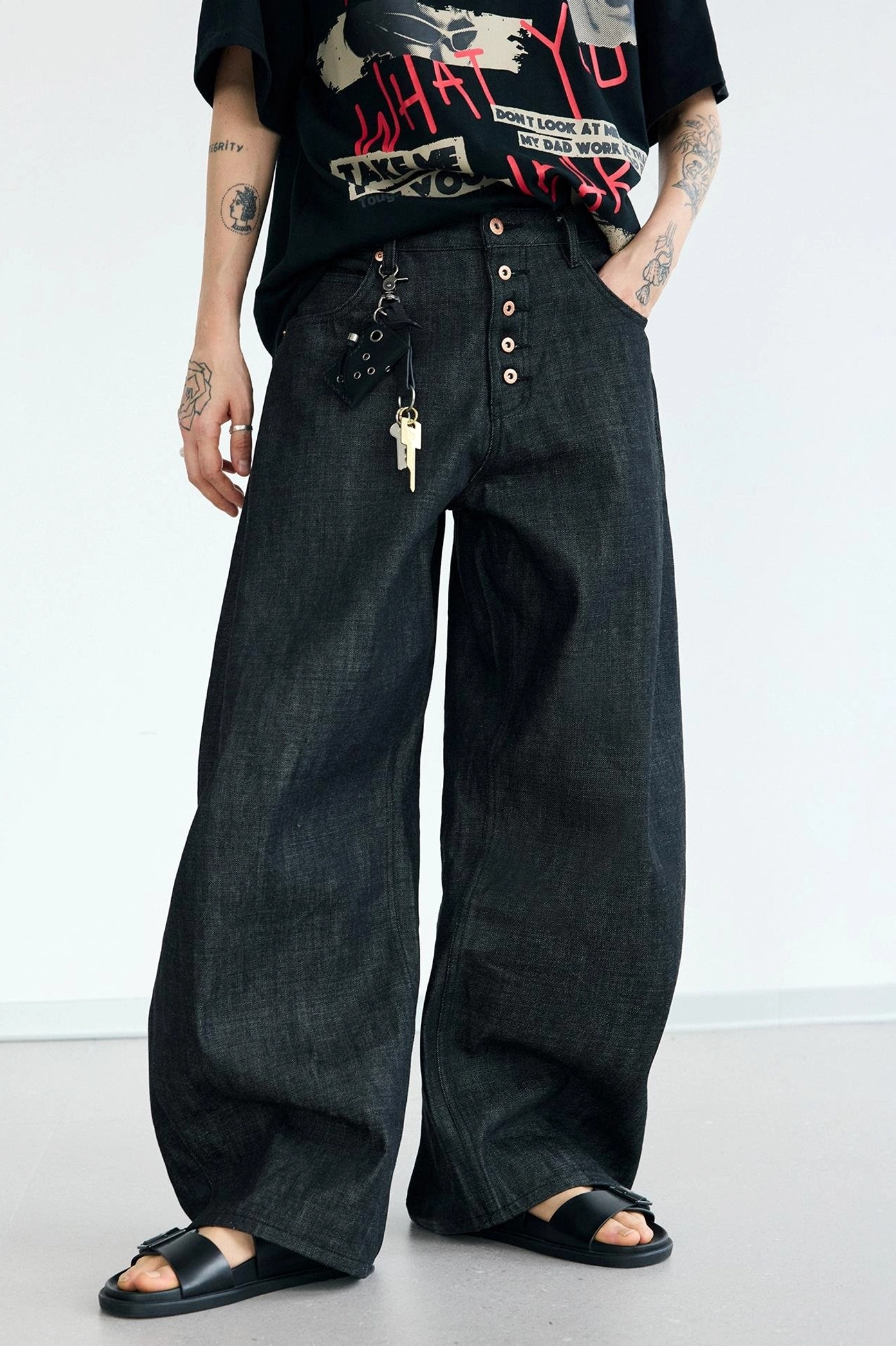 Front full-body view of men's black gold buckle wide-leg curved knife jeans with attached denim wallet keychain