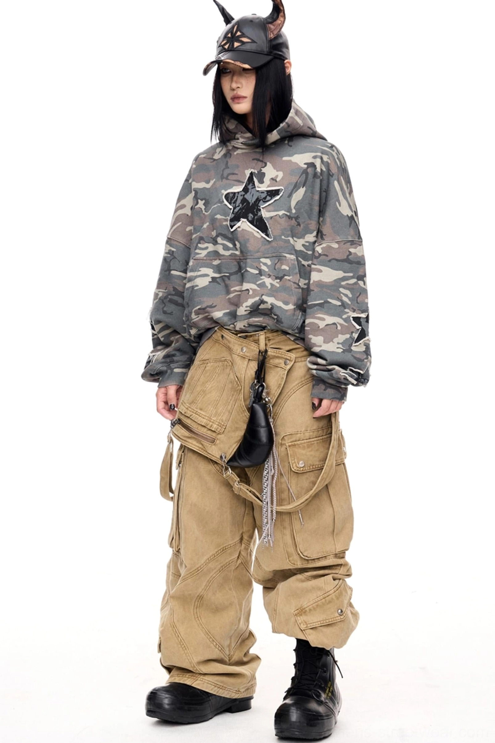 Full styling view of men's wide-leg detachable cargo pants with the removable pocket panel worn at the hip, camo hoodie, cap, and combat boots