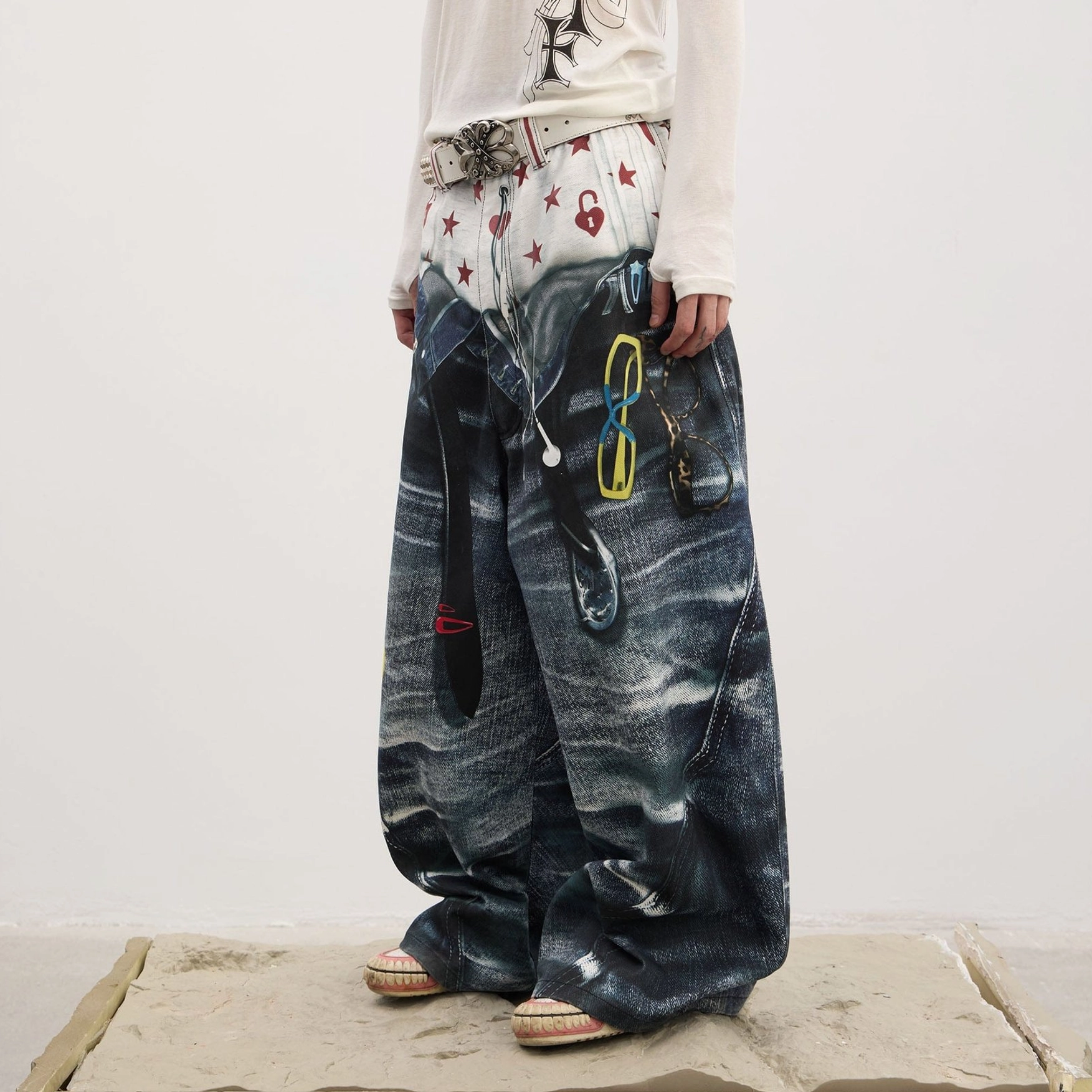 Side front detail of men's Y2K sagging-illusion jeans with printed star and heart waistband, hanging metal clip decorations, and loose wide-leg fit