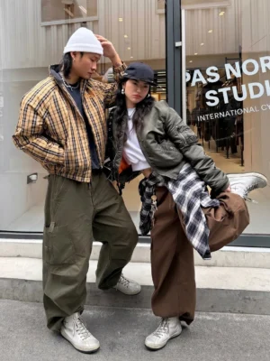 Two streetwear models wearing metallic grey lace-up ankle boots with casual urban outfits outside a contemporary clothing storefront