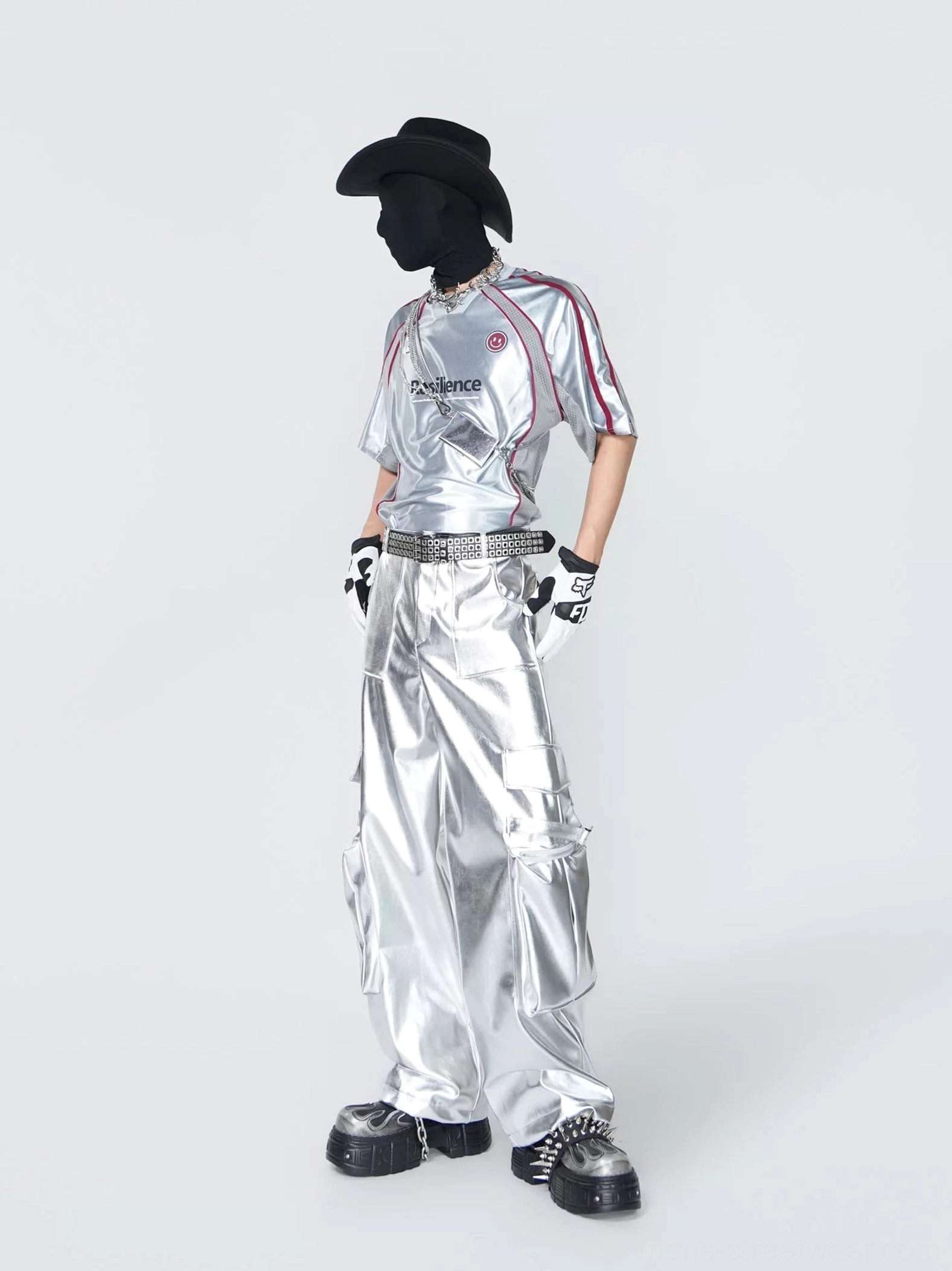 Side front view of a shiny silver athletic jersey top with red shoulder trim styled with futuristic cargo pants and streetwear accessories