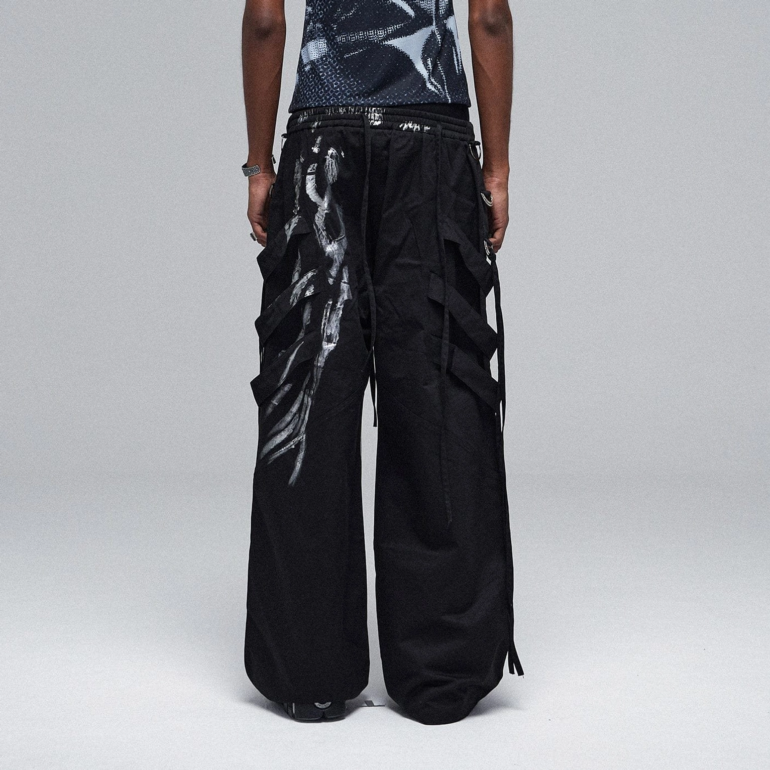 Back view of oversized black metallic strap cargo pants showing adjustable drawstring waist, rear strap details, and relaxed wide-leg silhouette