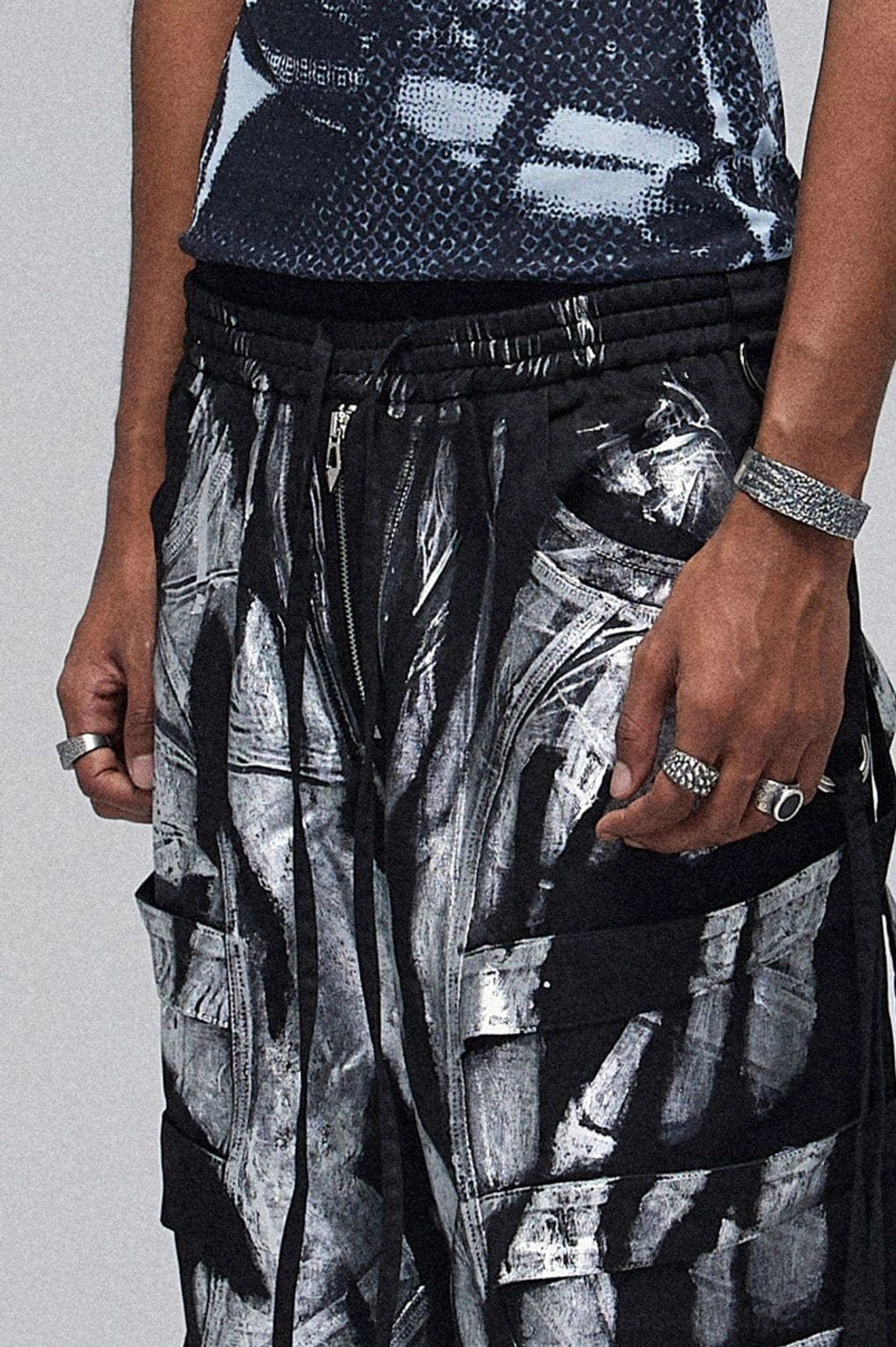 Close-up of metallic strap graffiti cargo pants waist and stacked cargo pockets with drawstring closure and silver abstract print
