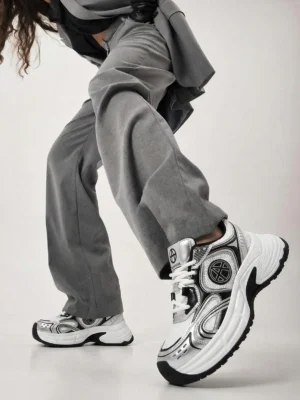 Model wearing Metallic Wave Chunky Dad Sneakers with gray loose wide-leg pants showing real world streetwear styling lower body dynamic pose