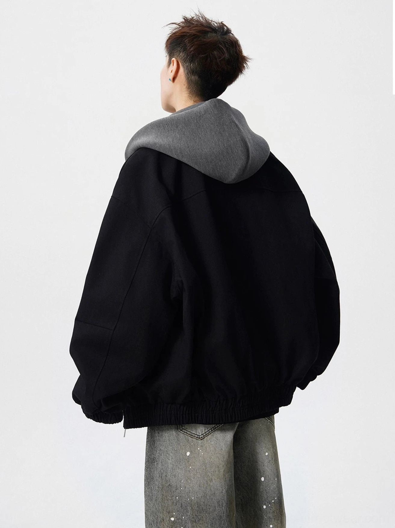 Back view of oversized black streetwear bomber jacket showing grey hood insert and relaxed silhouette