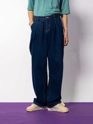 Front full-body view of dark indigo pleated wide-leg jeans styled with a teal streetwear top and beige sneakers