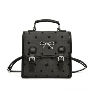 Front view of a dark grey polka dot bow satchel backpack with black faux leather trim, silver bow ornament, top handle, and convertible shoulder straps