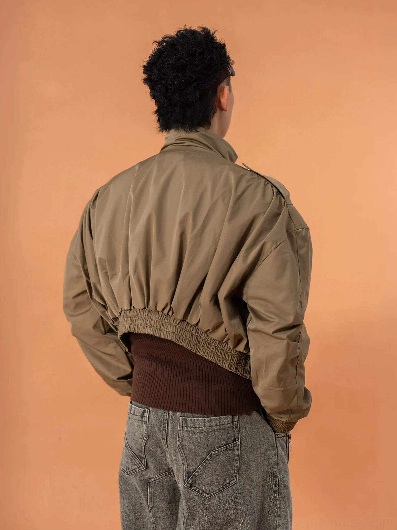 Back view of a military green cropped bomber jacket showing the relaxed batwing sleeves gathered elasticated hem and military shoulder epaulet details