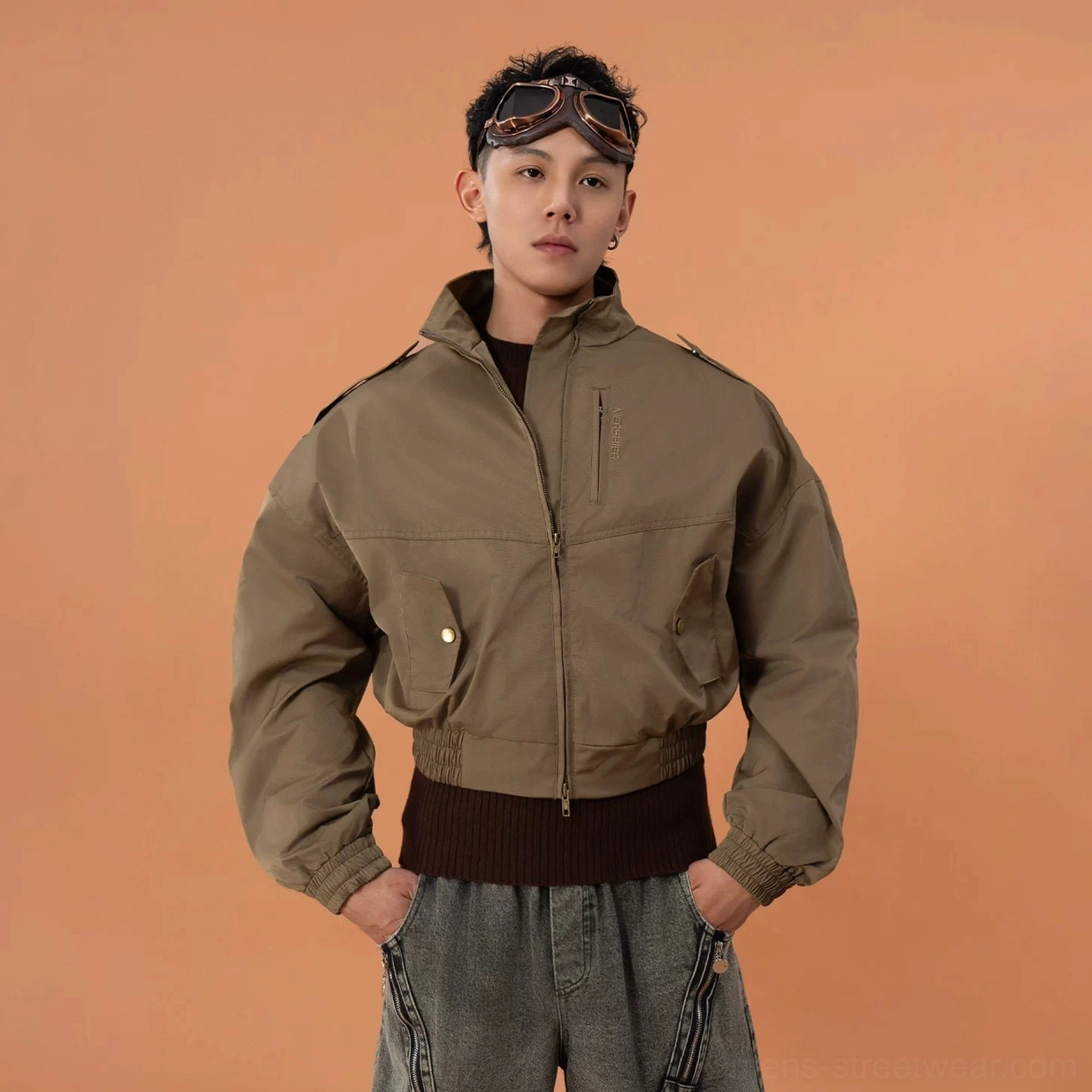 Front low-angle view of a military green cropped bomber jacket featuring full zip closure chest snap pocket ribbed cuffs and military streetwear styling