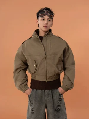 Front view of a military green cropped bomber jacket with stand collar shoulder epaulets zip front chest snap pockets ribbed cuffs and wide cropped hem styled with brown knit and wide-leg jeans