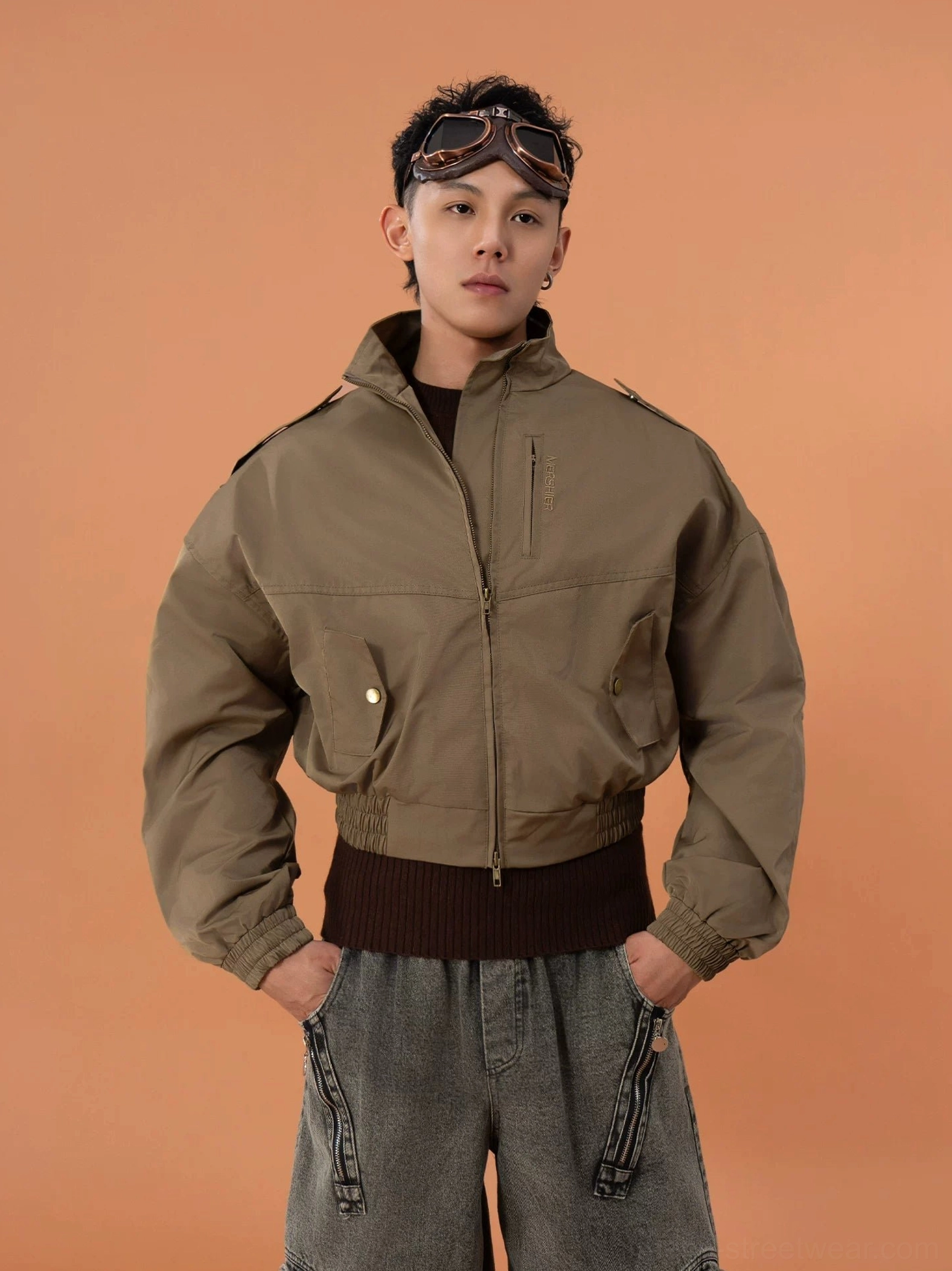 Front view of a military green cropped bomber jacket with stand collar shoulder epaulets zip front chest snap pockets ribbed cuffs and wide cropped hem styled with brown knit and wide-leg jeans