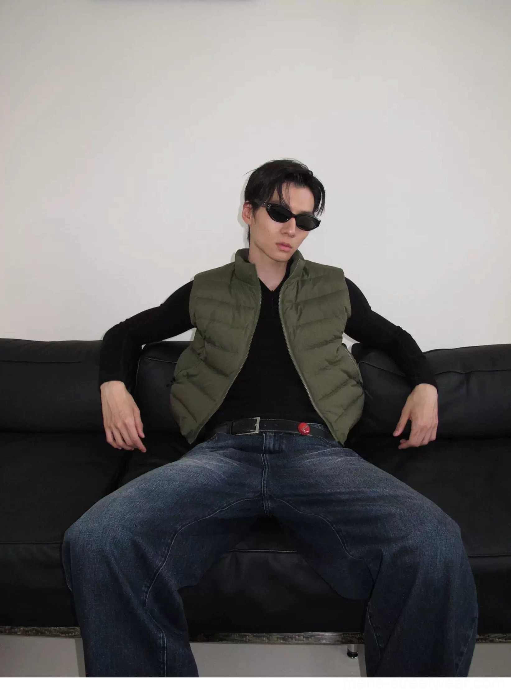 Military green quilted puffer vest with stand collar styled over a black fitted top in a seated studio look