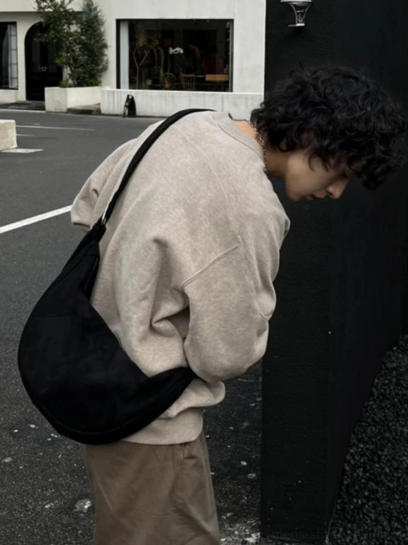 Minimal black half-moon crossbody sling bag rear side view styled with relaxed everyday streetwear at night