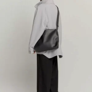 Black minimalist PU leather tech sling bag worn crossbody from the back with a light gray streetwear outfit