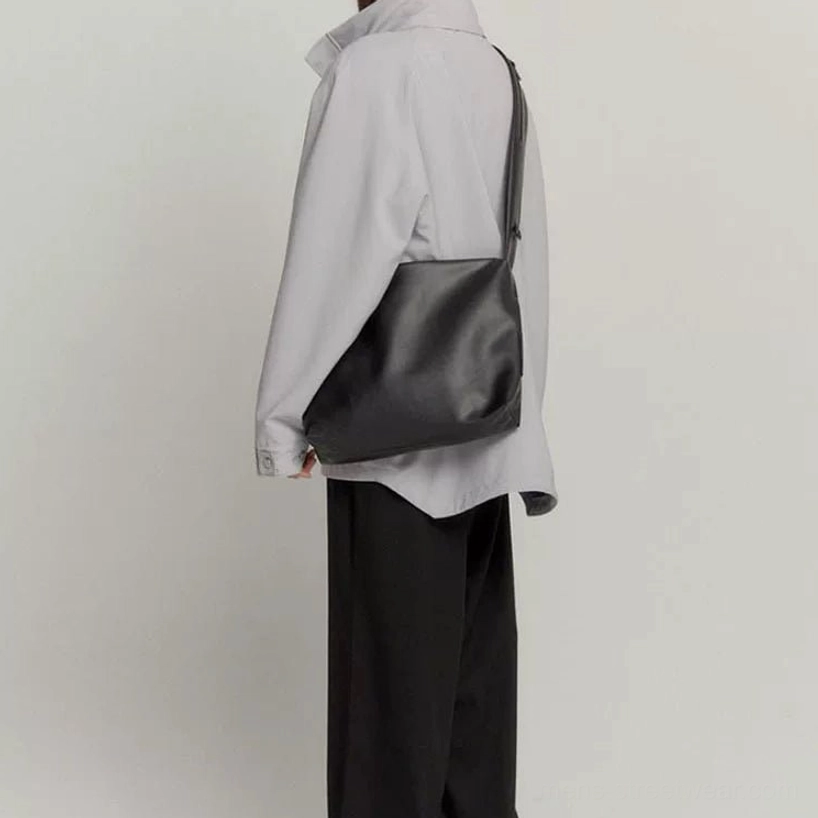 Black minimalist PU leather tech sling bag worn crossbody from the back with a light gray streetwear outfit